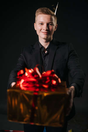 Man hands offer to take a gift in a colorful holiday package, close-up. Man dressed in a nice suit....