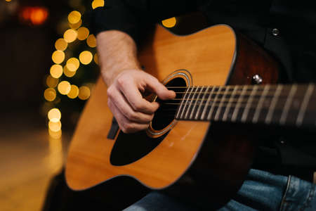 Man plays guitar close-up. Against the background of a decorated Christmas tree with a bokeh effect.の写真素材