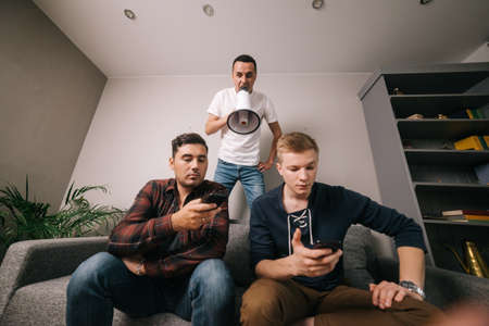 Young man yelling through a loudspeaker at friends which using a mobile phone.