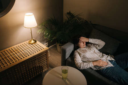 Unhealthy beautiful young woman lying on a sofa in a dark room. Top view.