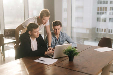 Team of young sturtupers discussing project or idea at the table with laptop in company meeting...