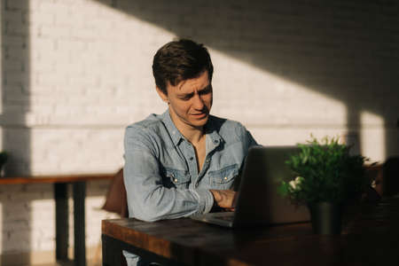 Pensive young business man sitting on chair and uses laptop n the office .