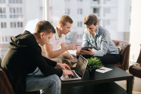 Friendly creative colleagues team discuss the project using a laptop and tablet in modern office....