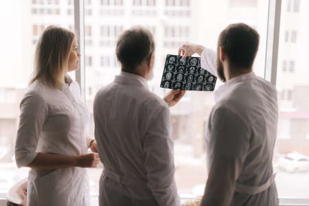 Team of three doctors discusses the results of an MRI scan of the patients head in the consulting...