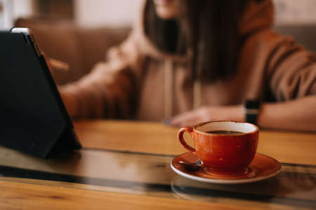 Close-up of a cup of dark coffee on a table in a cafe. In the background sits a unrecognizable young...