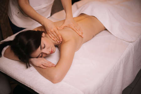 Female masseuse does shoulder and back massage to young woman in spa centre, close-up. Beautiful girl with perfect skin gets relaxing massage. Concept of professional massage. Concept of body care.の写真素材