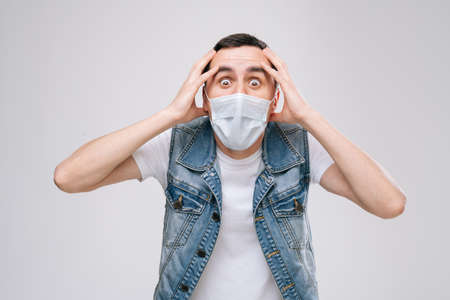 Scared man in medical mask afraid of something and looks into camera with big eyes full of horror,...
