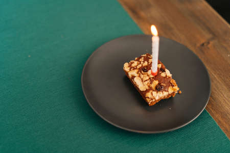 Close-up cake with burning candle in the bright room on dark plate, no people.の写真素材