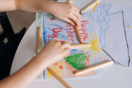 Close-up of childs hand drawing with colored pencils at the table in cozy childrens room. Concept of child creative activity.の写真素材