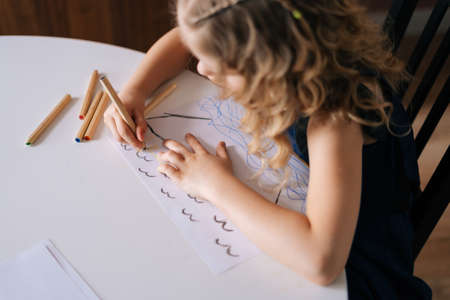 Adorable kid girl drawing with colorful pencils on paper at home, top view, back view. Concept of child creative activity.の写真素材