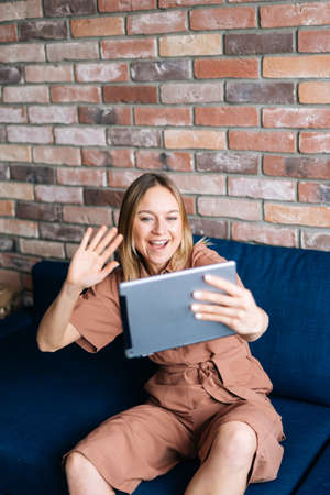 Beautiful young woman using her digital tablet with smile while sitting on soft couch in cozy living...