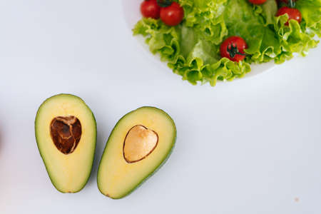 Fresh ripe sliced avocado cut in half on white table, salad leaves in the background. Concept of...