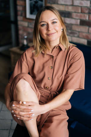 Woman sitting in a comfortable chair in dark living room, looking at the camera. Concept of home...