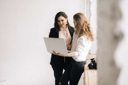 Two businesswomen work with laptop computer together against the window. Two business people working on laptop. Concept of teamwork young businessperson.の写真素材