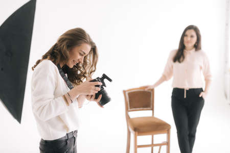 Portrait of young beautiful woman checks the pictures on the camera screen in light photo studio, on...