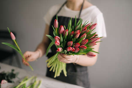 Unrecognizable young woman florist wearing apron making floral composition from fresh roses at the table on white background. Concept of working with flowers, floral business.の写真素材