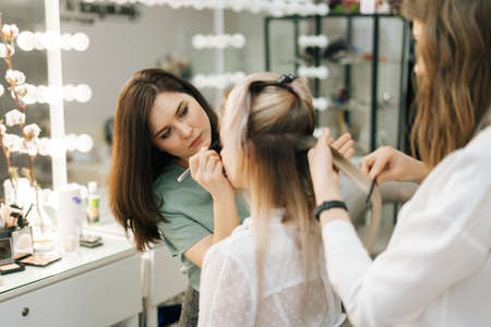 Two female make-up artist working with young woman model in dressing room. Concept of backstage work.の写真素材
