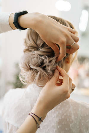Close-up of hands of hairdresser making hairstyle unrecognizable young blonde woman in beauty salon, back view. Concept of beauty, fashion and stylish makeup.の写真素材