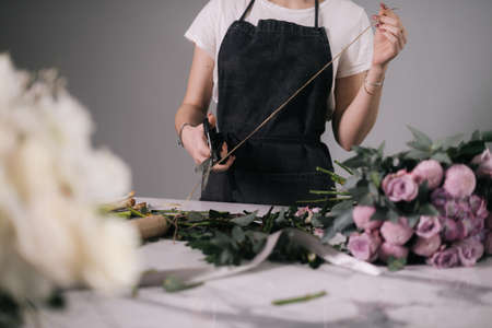 Middle shot portrait of woman florist cutting rope for wrapping bouquet of flowers at the table on...
