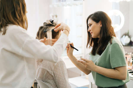 Two make-up artistes applies hair and makeup to the bride in dressing room. Concept of backstage work.の写真素材