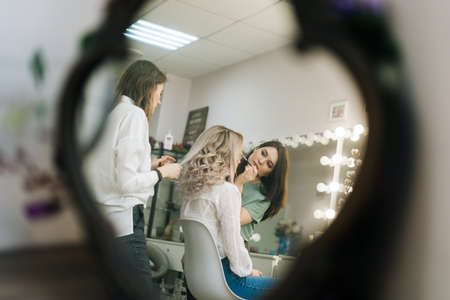 Two professional female make-up artist doing makeover in lighting dressing room, view from afar. Concept of backstage work.の写真素材