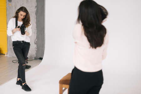 Woman photographer and female model together looking at made photo and talking,smiling, white background. Concept of creative work in photo studio, backstage job.の写真素材