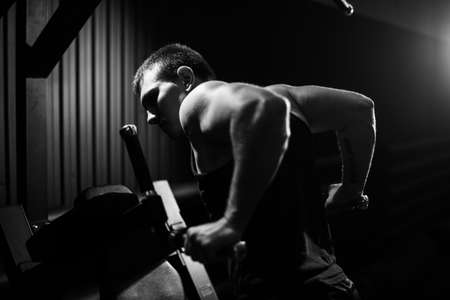 Muscular young man with perfect beautiful body wearing sportswear doing push-ups on bars during...