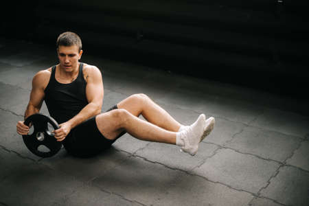 Healthy lifestyle athletic man doing russian twist exercise with weight from barbell on black mat during sport workout training in modern gym. Concept of healthy lifestyle, physical sport activity.の写真素材