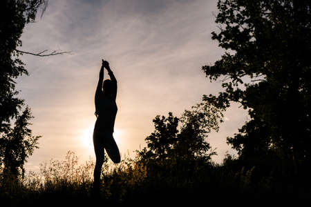 Silhouette of woman doing yoga in evening outdoors background of setting sun. Girl is performing...