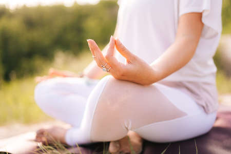 Close-up of unrecognizable woman sitting in lotus position and holding her finger hand in Om...