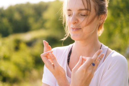 Close up portrait of face of calm young meditating woman standing on nature with closed eyes holding...