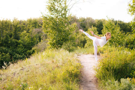 Happy lady practicing yoga, standing in Warrior three exercise, Virabhadrasana III pose. Athletic lady doing warrior yoga asana pose outside, nature. Concept of practicing yoga alone outdoor.の写真素材