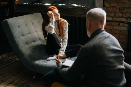 Depressed red-haired young woman talking about her problems at psychologist appointment....