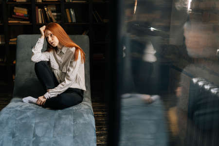 Attractive depressed red-haired young woman patient sitting on comfortable armchair and telling about her problems to psychotherapist. . Concept of psychological treatment.の写真素材