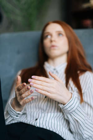Close-up view of sad red-haired young woman talking about problems at psychologist appointment....