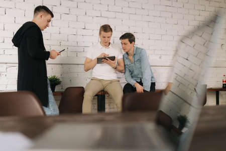 Business team young men of startupers rest during break background of white brick wall. Guy shows...