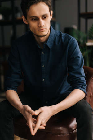 Portrait of handsome thoughtful young business man with pensive expression sitting at the chair in...