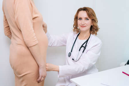Smiling doctor in white coat measure belly waist size of unrecognizable pregnant young woman using...