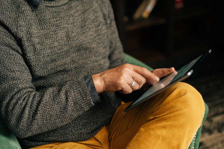 Close-up of hands of unrecognizable senior adult male browsing internet content using digital...