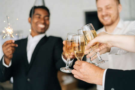 Close-up view of business team of multinational employees holding Bengal lights, clinking glasses of champagne and smiling cheerfully at corporate New Year or Happy Christmas eve.の写真素材