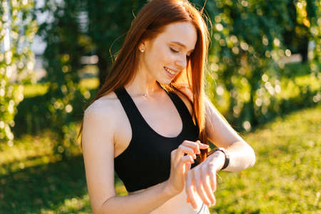 Close-up portrait of young smiling woman touch on the screen of the smart watch on her wrist to...