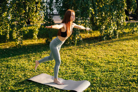 Sporty young woman with closed eyes practicing yoga standing with hands divorced to side and deeply...