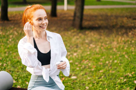 Close-up portrait of face of happy young woman putting on wireless earphones. Lady runner is preparing for morning or evening jogging. Concept of healthy lifestyle and sports training alone in air.の写真素材