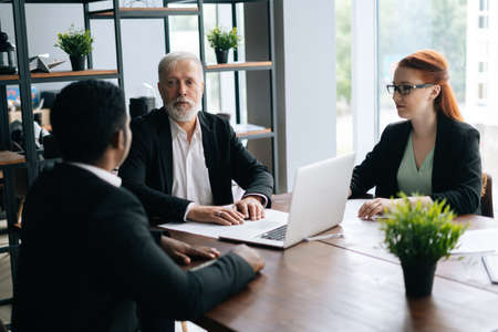 Skilled mature adult male businessman having meeting with young diverse multi-ethnic business...