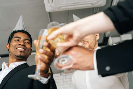 Close-up view of business team of multinational employees holding clinking glasses of champagne and smiling cheerfully at corporate New Year or Happy Christmas eve.の写真素材