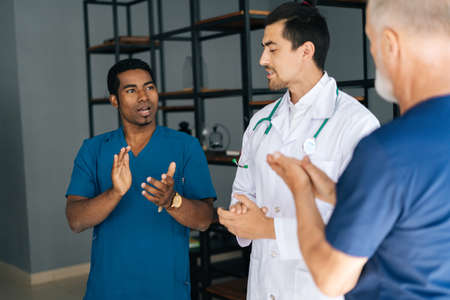 Mixed-races team of male doctors applauding in hospital. Group of multi-ethnic of doctors clapping...