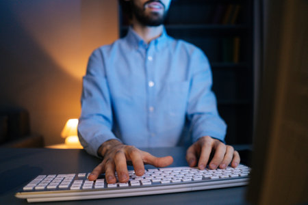 Close-up view of hands of unrecognizable man using computer typing message on wireless keyboard at dark room. Closeup of working on pc. On monitor screen change of images. Concept of remote working.の写真素材
