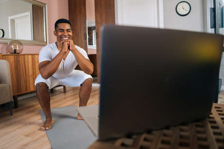 Front view of cheerful muscular African-American man wearing white T-shirt exercising and doing...