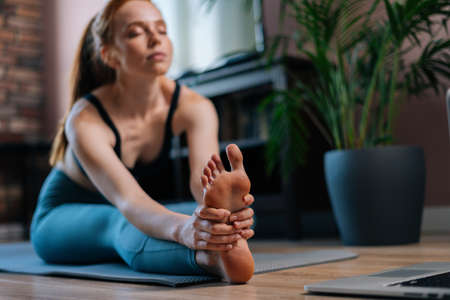 Close-up of flexible redhead young woman working out, doing stretching exercise on yoga mat while...