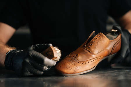 Close-up front view of unrecognizable shoemaker cleaning with brush old light brown leather shoe....